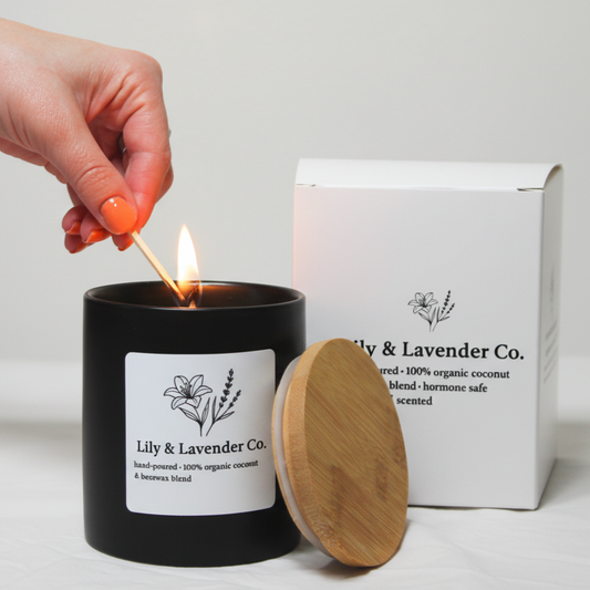 Lily & Lavender Co. Non-Toxic Coconut Wax & Beeswax Candle being lit with a match, next to box package.