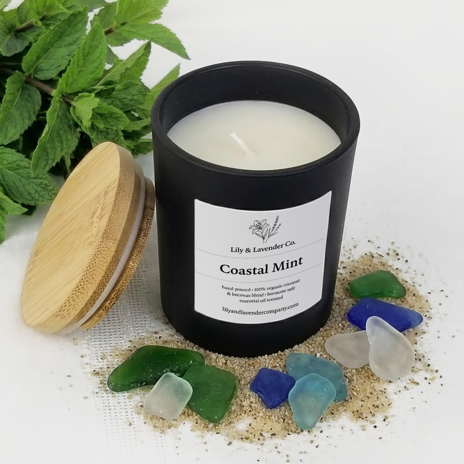 Lily & Lavender Co. Coastal Mint, Essential Oil Scented, Non-Toxic Coconut & Beeswax Candle 6oz with a bushel of Mint, beach sand, and sea glass on a white background.