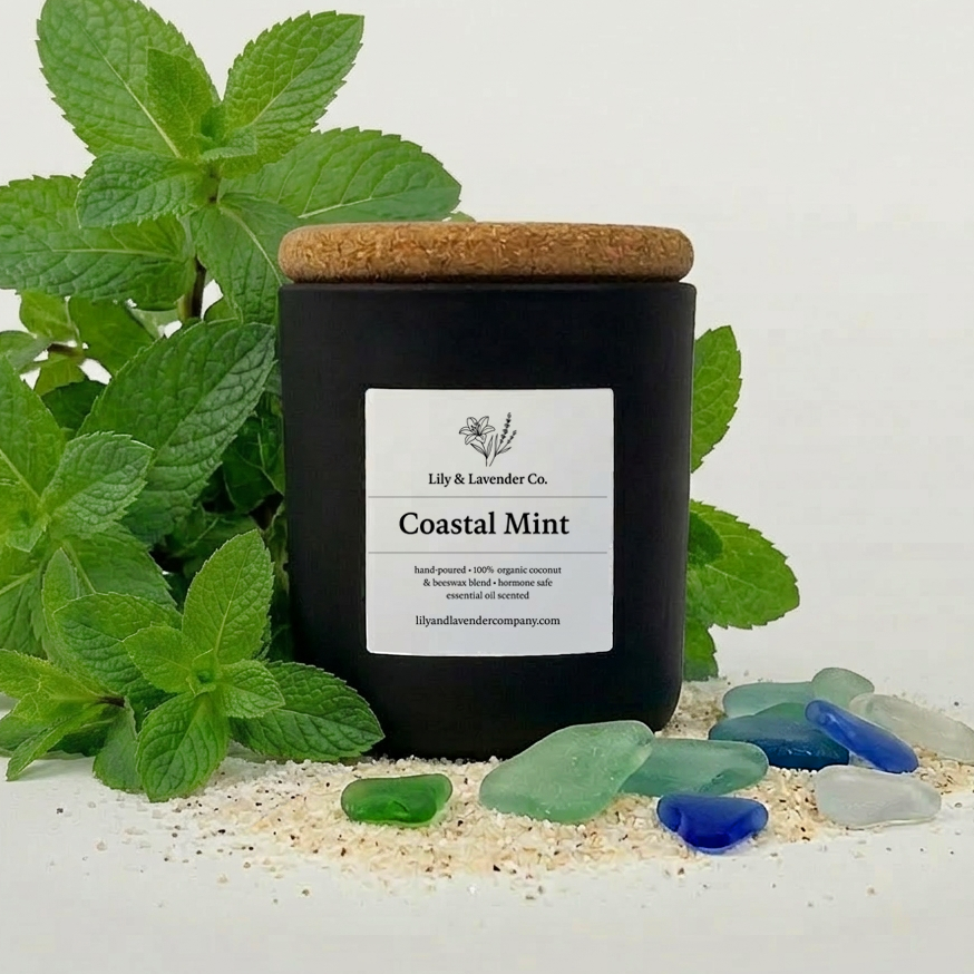Lily & Lavender Co. Coastal Mint, Essential Oil Scented, Non-Toxic Coconut & Beeswax Candle 4oz with a bushel of Mint, beach sand, and sea glass on a white background.