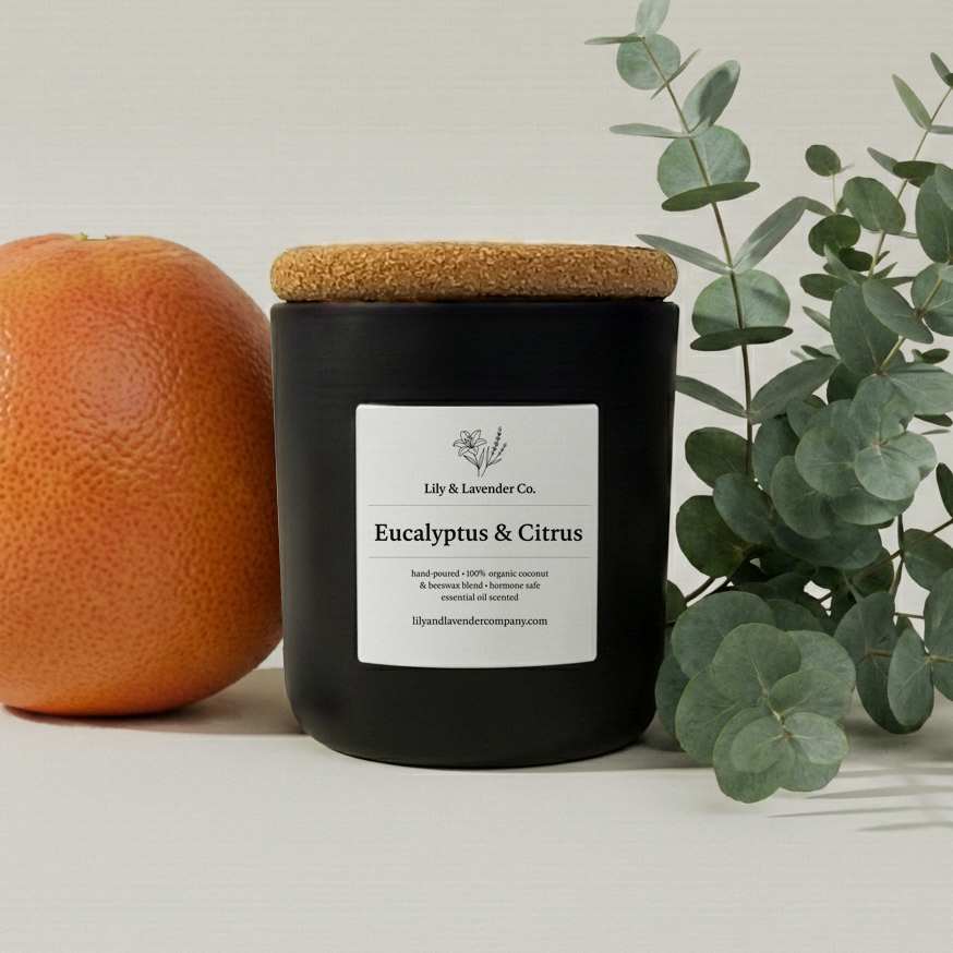 Lily & Lavender non-toxic, candle with cork lid labeled 'Eucalyptus & Citrus' next to a grapefruit and eucalyptus leaves on a light background