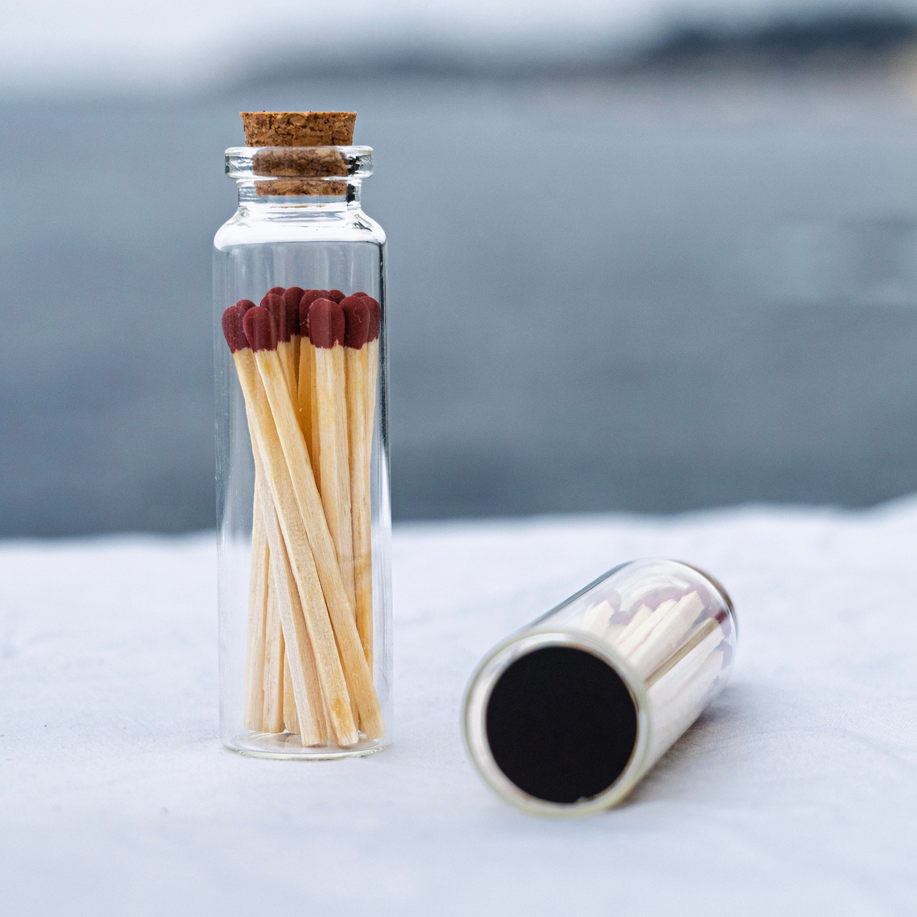 Glass bottle with matches on a white surface with the ocean in the background