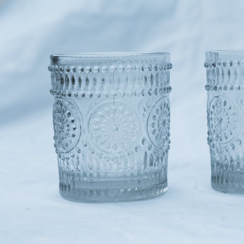 Two clear glass votives with decorative patterns on a white background