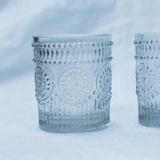 Two clear glass votives with decorative patterns on a white background